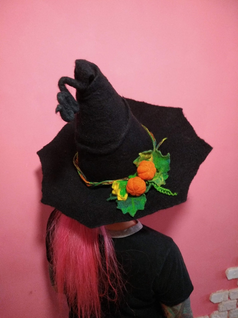 May include: A black witch hat with a wide brim and a tall pointed crown. The hat is decorated with a green felt vine and three orange felt pumpkins.