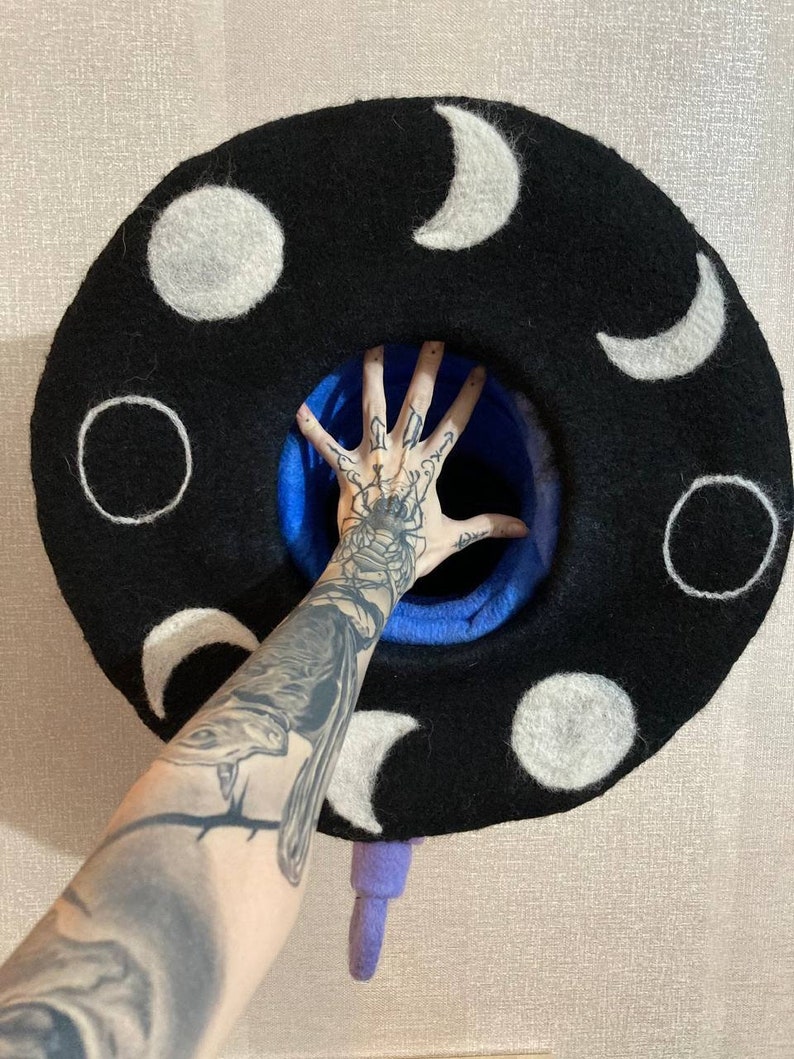 May include: A black felt hat with white moon phases embroidered on it. The hat has a blue lining and a purple tassel.