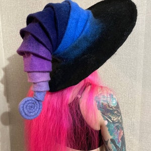 May include: A large, wide-brimmed hat made of felt with a gradient of purple, blue, and black colors. The hat has a unique, spiral-shaped design on the side.