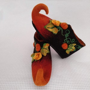 May include: A pair of orange and black felt slippers with a pumpkin design. The slippers have a pointed toe and a curled up toe.