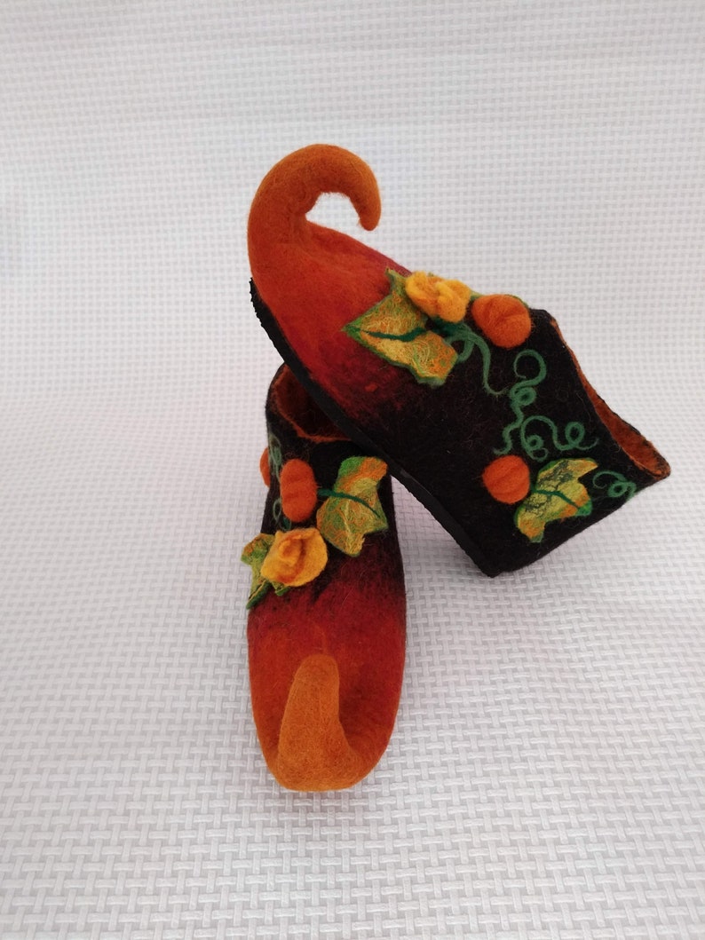 May include: A pair of orange and black felt slippers with a pumpkin design. The slippers have a pointed toe and a curled up toe.
