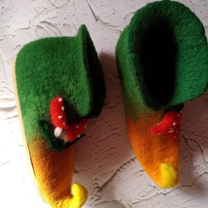 May include: A pair of green and yellow felt slippers with red mushroom accents. The slippers have a pointed toe and a curled up heel.