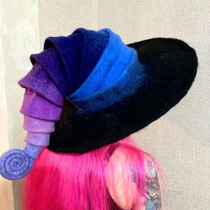 May include: A large, wide-brimmed witch hat with a curled, purple, blue, and black ombre felt brim. The hat has a long, curled felt tail that is also ombre in shades of purple and blue.
