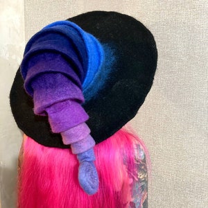 May include: A black felt witch hat with a tall, curled brim. The brim is a gradient of blue, purple, and pink.