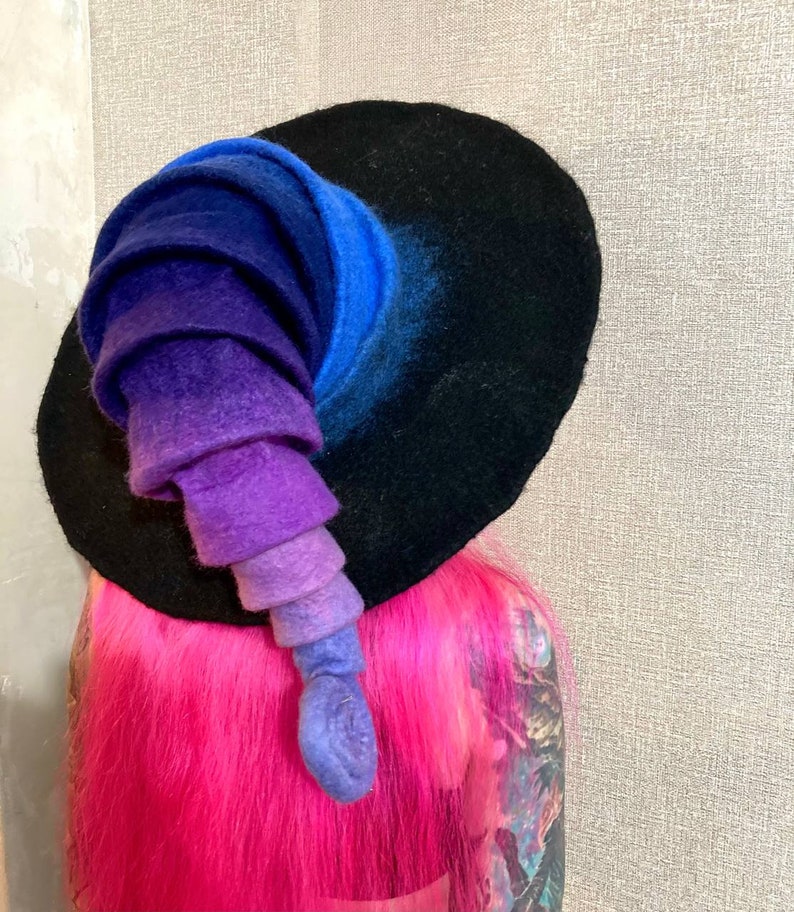 May include: A black felt witch hat with a tall, curled brim. The brim is a gradient of blue, purple, and pink.