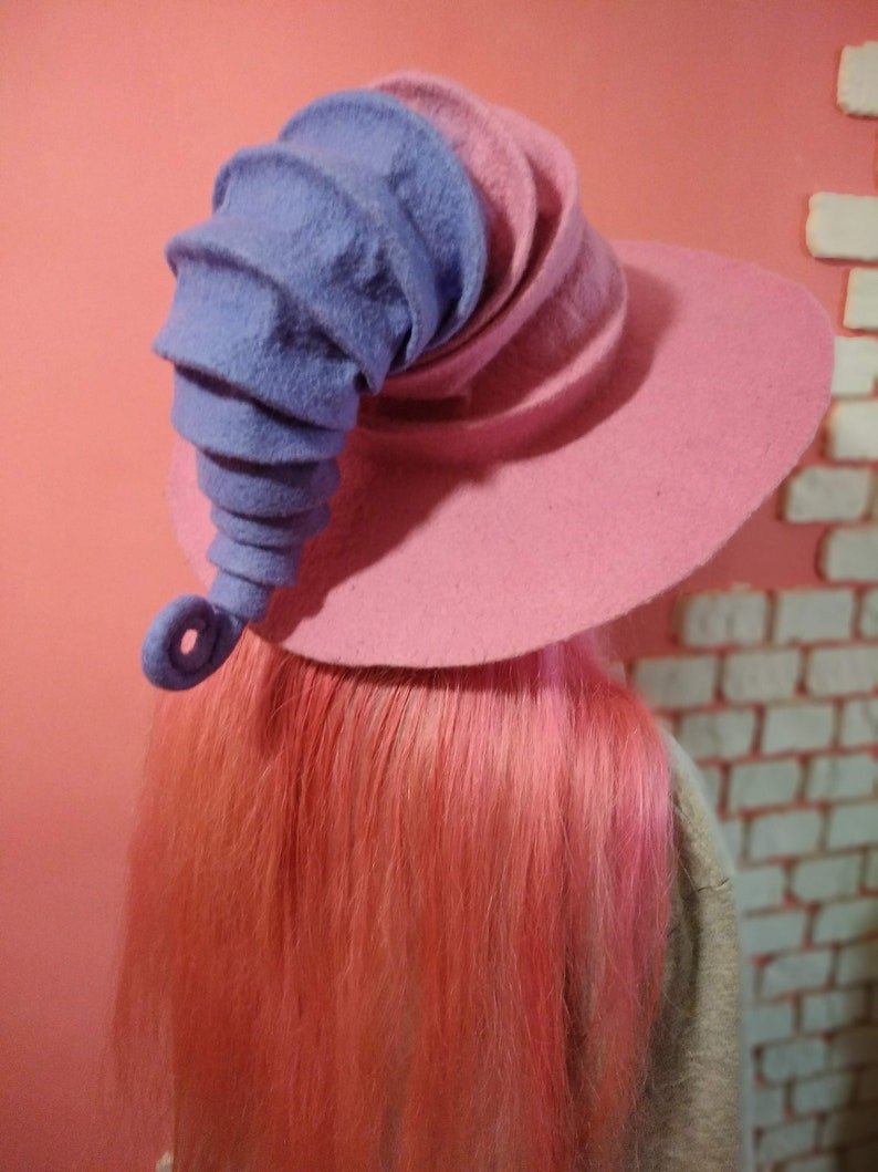 May include: A pink and purple felt witch hat with a curled brim and a tall, curled purple felt horn.