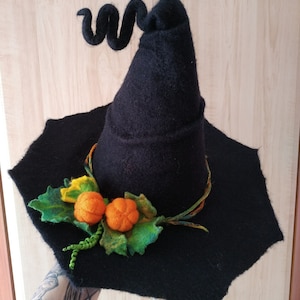 May include: A black felt witch hat with a curled brim and a pointed crown. The hat is decorated with a green felt leaf and two orange felt pumpkins.