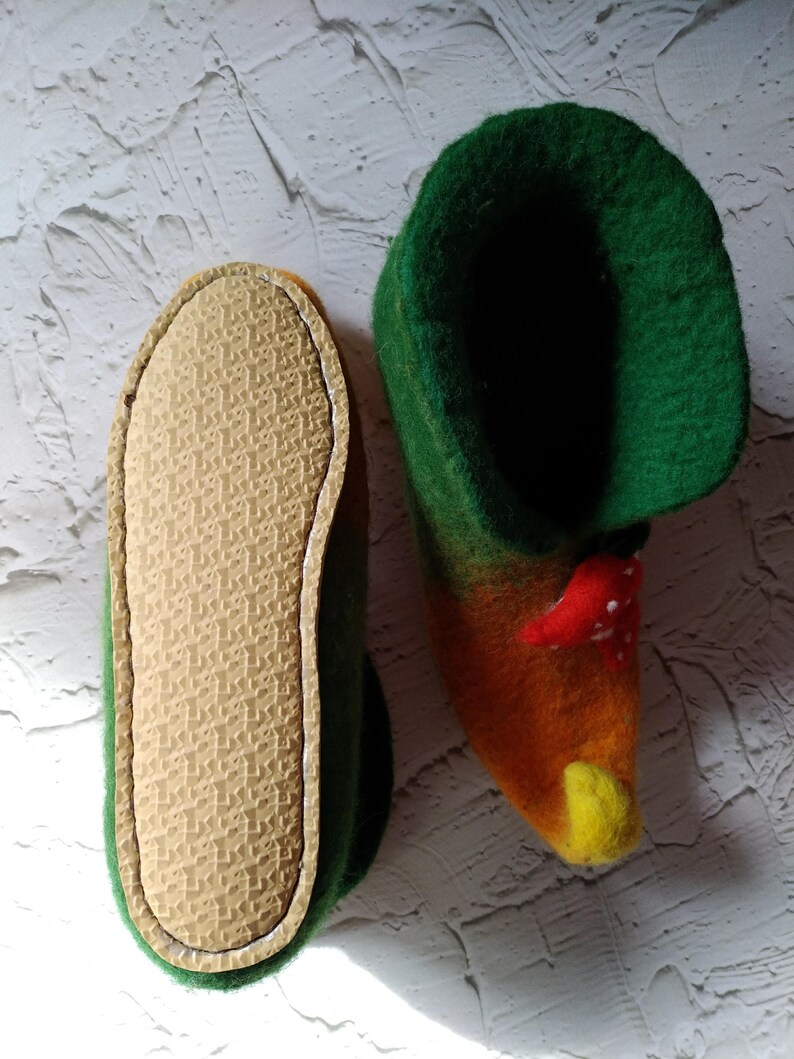 May include: A pair of green, orange, and yellow felt slippers with a mushroom design. The slippers have a brown rubber sole.