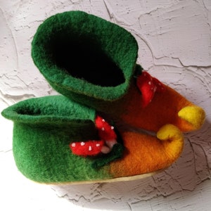May include: A pair of green and orange felt slippers with a mushroom design. The slippers have a pointed toe and a yellow curled toe.