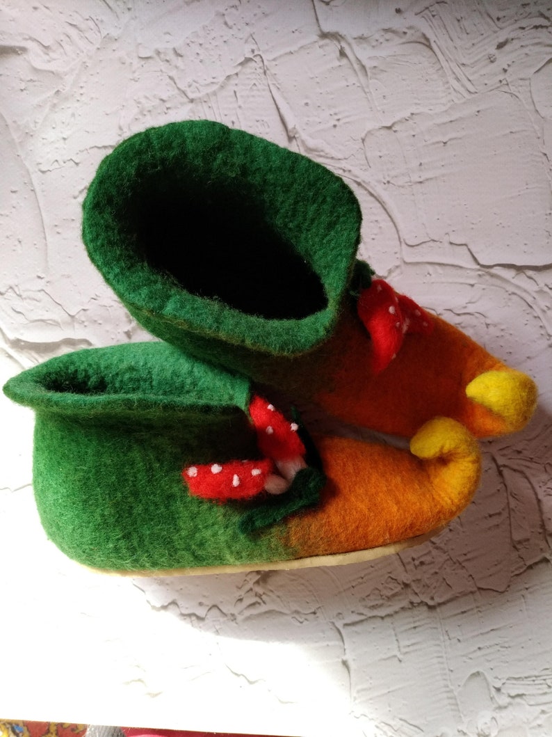 May include: A pair of green and orange felt slippers with a mushroom design. The slippers have a pointed toe and a yellow curled toe.