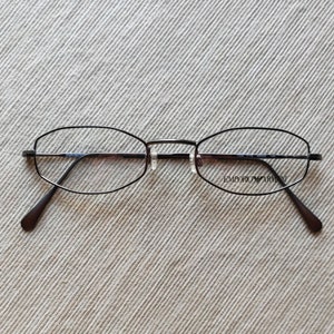 Könnte beinhalten: Schwarze Metallgestellbrille mit klaren Gläsern. Der Rahmen hat eine einzigartige Form und der Markenname "EMPORIO ARMANI" ist auf dem rechten Glas aufgedruckt.