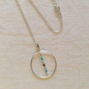 May include: A silver chain necklace with a circle pendant. The pendant has a vertical line of turquoise and silver beads inside.