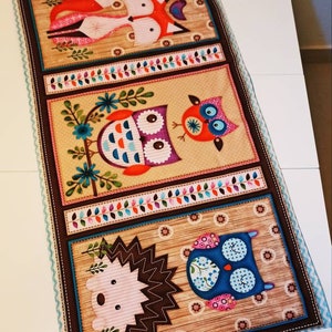 Könnte beinhalten: Ein braunes Stoffpanel mit drei bunten Tiermotiven. Das obere Motiv ist ein roter Fuchs, das mittlere Motiv ist eine blaue und orangefarbene Eule, und das untere Motiv ist ein rosa Igel und eine blaue Eule.