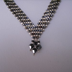 Puede incluir: Un collar de cuentas plateadas y negras con un diseño en forma de V y un colgante de cristal negro.