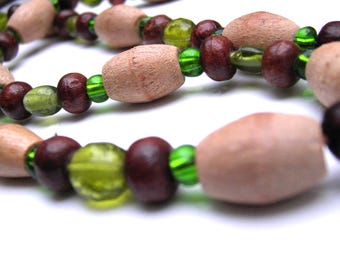 Puede incluir: Un collar que presenta un patrón repetitivo de cuentas de madera de color tostado claro en forma de barril, cuentas de madera esféricas de color marrón oscuro y cuentas de vidrio verde lima translúcido. Las cuentas están ensartadas.