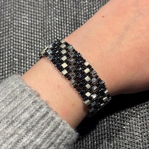Può includere: Un braccialetto con perline nere e argentate con un motivo geometrico. Il braccialetto è indossato al polso.