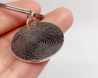 May include: Silver bracelet with a round charm featuring a detailed fingerprint design.