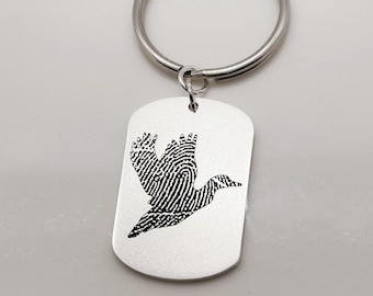 May include: Silver keychain with a doggo silhouette made from a fingerprint design. The keychain is attached to a silver key ring.