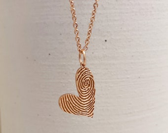 May include: A rose gold necklace with a heart-shaped pendant. The pendant is made of a fingerprint design.