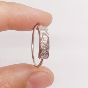 Könnte beinhalten: Ein silberner Ring mit einem Fingerabdruck-Design auf der Band.