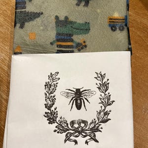 May include: A stack of Bellarine Bee Wraps. The top wrap has a light green background with cartoon alligators and train graphics. The bottom wrap is partially visible. The label features a bee illustration and the text "Bellarine Bee Wraps."