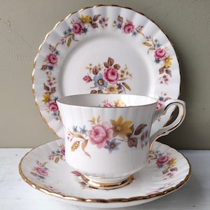 Peut inclure: Un ensemble de tasse à thé et soucoupe blanche avec un motif floral dans les tons de rose, bleu et jaune. L'ensemble est bordé d'une garniture dorée.