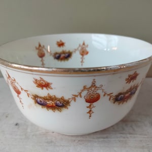 Puede incluir: Un azucarero de porcelana blanca con un borde dorado y un patrón floral en tonos naranja, marrón y morado.