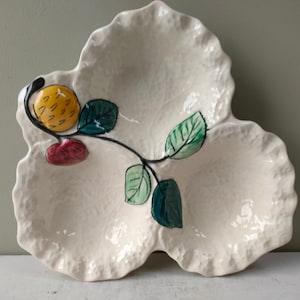 Puede incluir: Un plato de servir de cerámica blanca con tres secciones, cada una con forma de hoja. El plato está decorado con una vid pintada con hojas verdes y frutos rojos y amarillos.