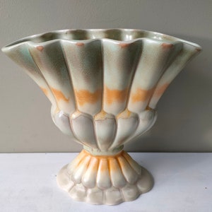May include: A large, ceramic vase with a scalloped rim and a fluted base. The vase is glazed in shades of green, orange, and white.