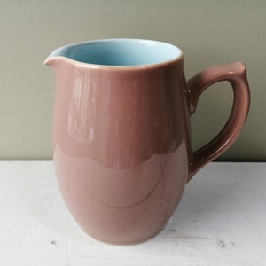 May include: A brown ceramic jug with a light blue interior. The jug has a rounded body and a handle.