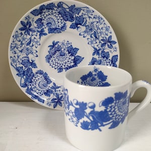 May include: A white teacup and saucer with a blue floral pattern. The pattern features blue flowers and leaves on a white background.