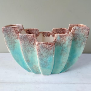 Könnte beinhalten: Ein türkisfarbener und brauner Keramik-Pflanztopf mit einem gewellten Rand. Der Topf hat eine einzigartige, organische Form und ist perfekt für die Präsentation von Pflanzen oder Blumen.