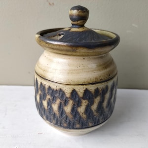 May include: A small ceramic jar with a lid, featuring a brown and white glaze with a black and white geometric pattern.