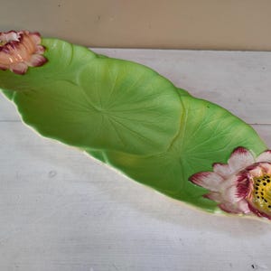 Puede incluir: Un plato de servir de cerámica verde con forma de hoja de nenúfar con dos flores de nenúfar rosas y blancas.