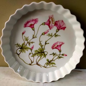 May include: White ceramic pie dish with a scalloped edge. The dish is decorated with pink morning glory flowers and green leaves. A decorative serving piece for the kitchen.