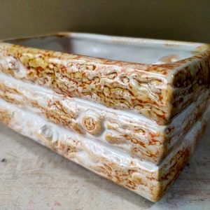 May include: A white ceramic planter with a brown wood grain design. The planter is rectangular and has a slightly rounded bottom.