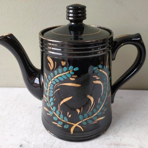 May include: Black teapot with a gold and teal floral design. The teapot has a lid and a spout.