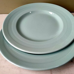 Può includere: Due piatti in ceramica azzurra sovrapposti. Ogni piatto ha un bordo largo con linee concentriche in rilievo. I piatti sono di colore pieno e opaco, con un centro leggermente concavo. Sono su una superficie di legno bianco.