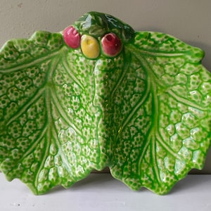 Puede incluir: Un plato de servir de cerámica verde con forma de hoja de lechuga con tres secciones. El plato tiene una superficie texturizada y está decorado con bayas rojas y amarillas.