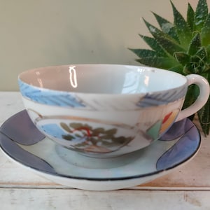 May include: A white teacup and saucer with a blue, yellow and red floral design. The saucer has a blue and white rim.