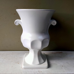 Op de afbeelding: Een witte keramische mok met een zwart handvat en de tekst "But First, Coffee" in een zwarte, vette letter. De mok staat op een wit oppervlak.