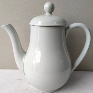 May include: A white ceramic coffee pot with a lid and a handle. The pot has a rounded body and a spout.