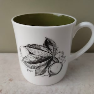 Puede incluir: Taza de cerámica blanca con interior verde y una ilustración en blanco y negro de una vid con la palabra "uva" impresa en el lateral.