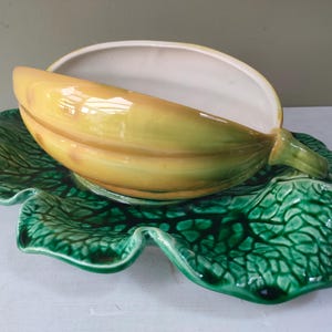 以下が含まれることがあります： 緑の葉のベースが付いたバナナの形をしたセラミック製のサービングディッシュ。バナナは黄色と緑で、内側は白です。