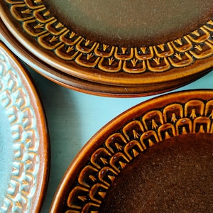 Puede incluir: Vista aérea de varios platos de cerámica. Los platos son marrones y turquesas con un patrón decorativo alrededor de los bordes. Los platos marrones están apilados y el plato turquesa está a la izquierda.
