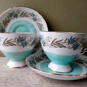Op de afbeelding: Twee theekopjes en schoteltjes met een blauw en wit bloemenpatroon. De kopjes en schoteltjes hebben een gouden rand.
