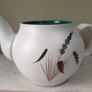 May include: White teapot with a green rim and a floral design featuring green, red, and yellow accents.