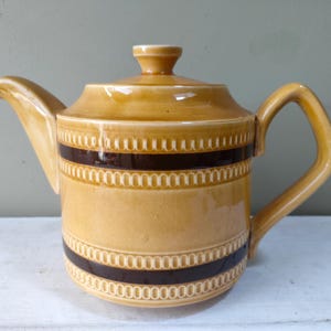May include: A brown ceramic teapot with a brown and white patterned design. The teapot has a wide spout and a handle.