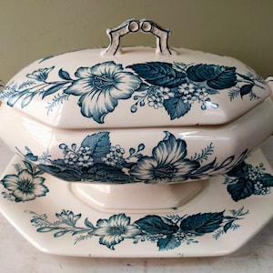 Puede incluir: Fuente de cerámica color crema con tapa y base a juego, decorada con motivos florales azules. El plato tiene un asa en la tapa y asas laterales. La base es octogonal. Una pieza clásica para servir alimentos.