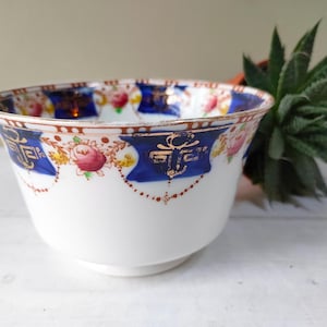 Puede incluir: Un tazón de porcelana blanca con un diseño floral azul y dorado. El tazón tiene un borde festoneado y una base ancha.